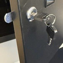 Close-up of a chrome-plated cylinder lock with a black key inserted into a black cabinet door, with an extended silver lockin