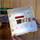 White plastic enclosure for electrical installation, held by hands against a wooden wall with electrical components. Red part