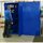 Blue metal storage cabinet with one door open, showing shelves with tools and cans. A person stands by the cabinet in a works